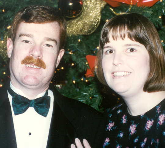 tuxedoed man and his wife in front of a Christmas tree